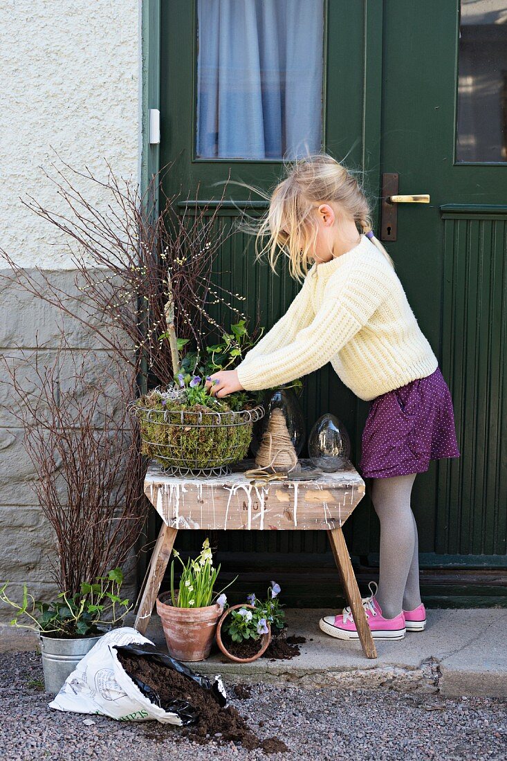 Girl planting arrangement of pussy willow and spring plants in wire basket
