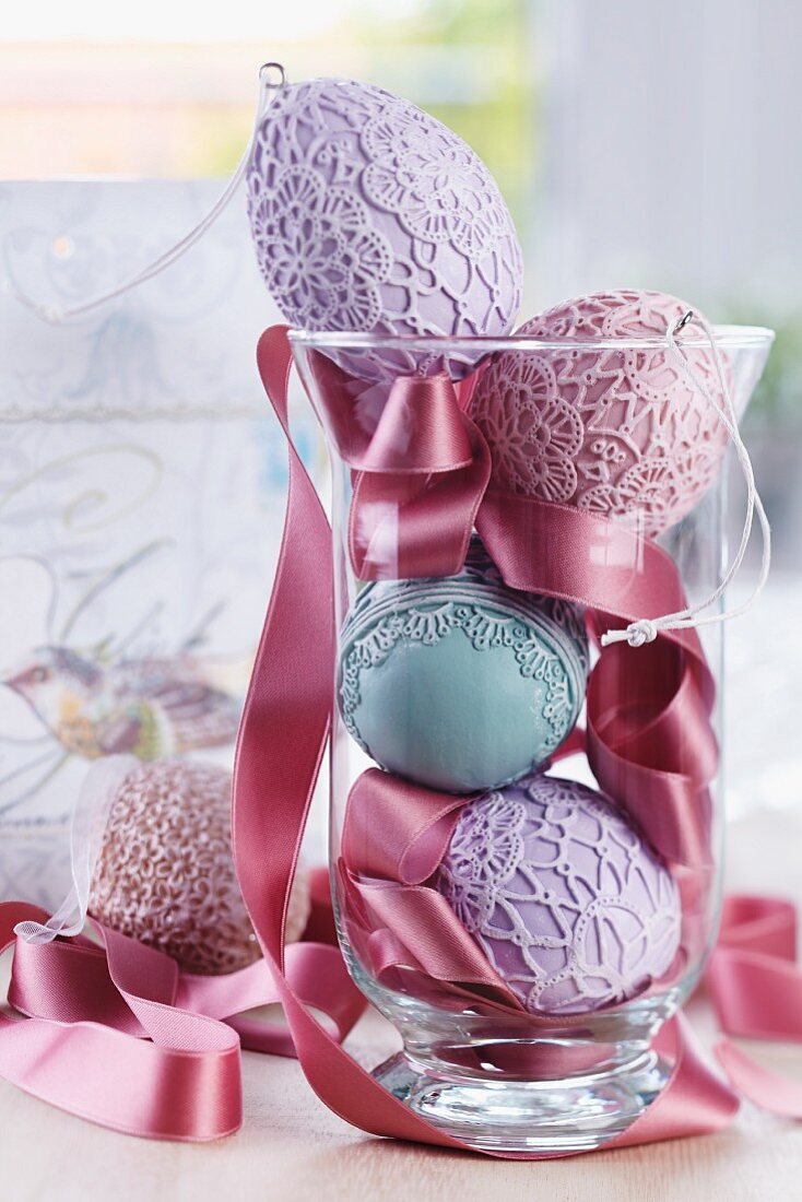 Easter arrangement of ceramic eggs with various lacy patterns and satin ribbon in glass vase