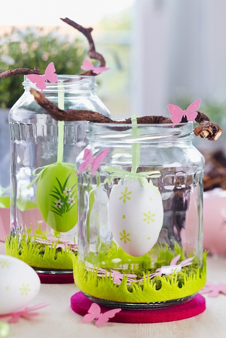 Easter table decorations with Easter eggs hanging from twigs in screw-top jars