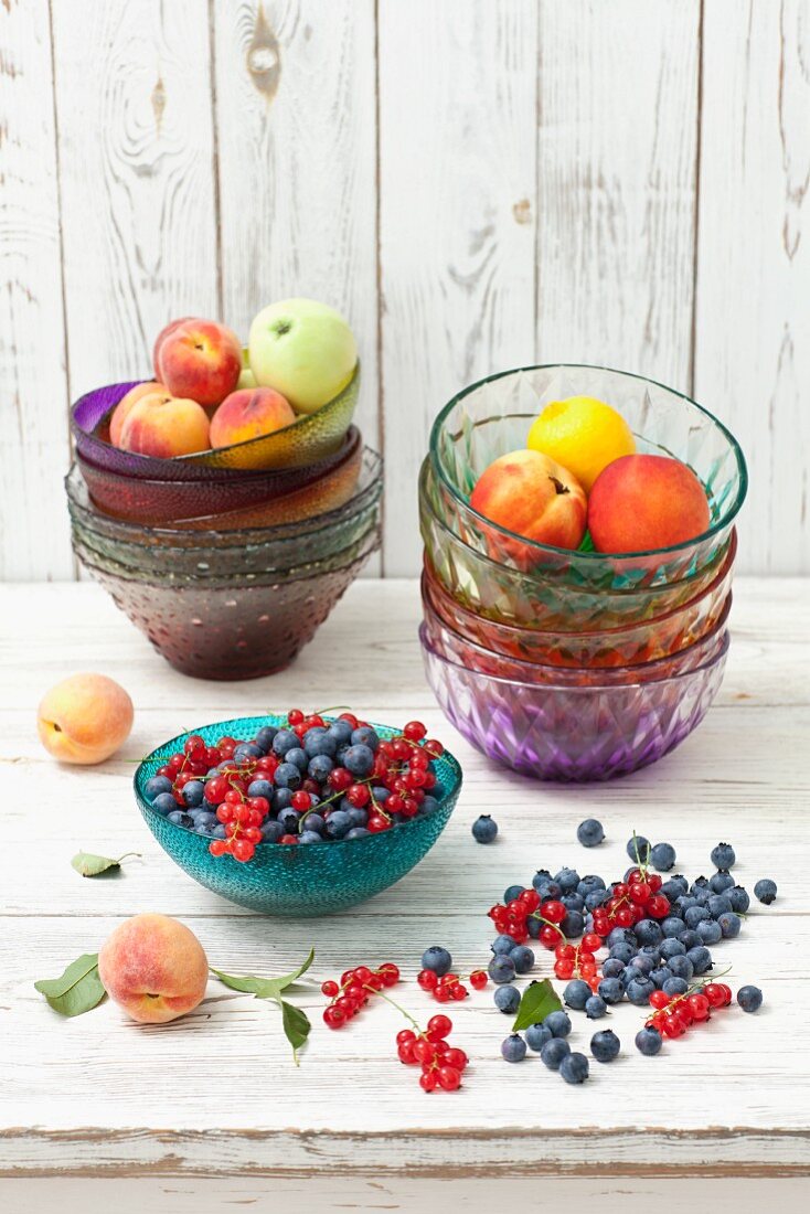 Blueberries, redcurrants, peaches, apples and lemons in glass bowls