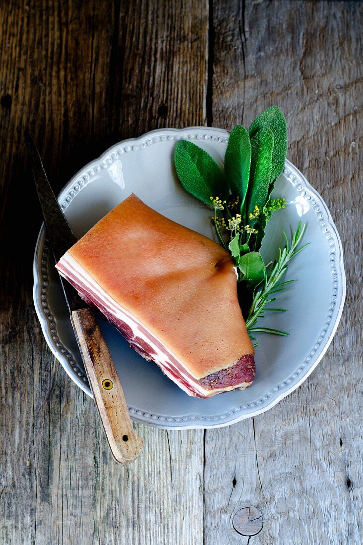 Pancetta mit Messer und frischen Kräutern auf Teller