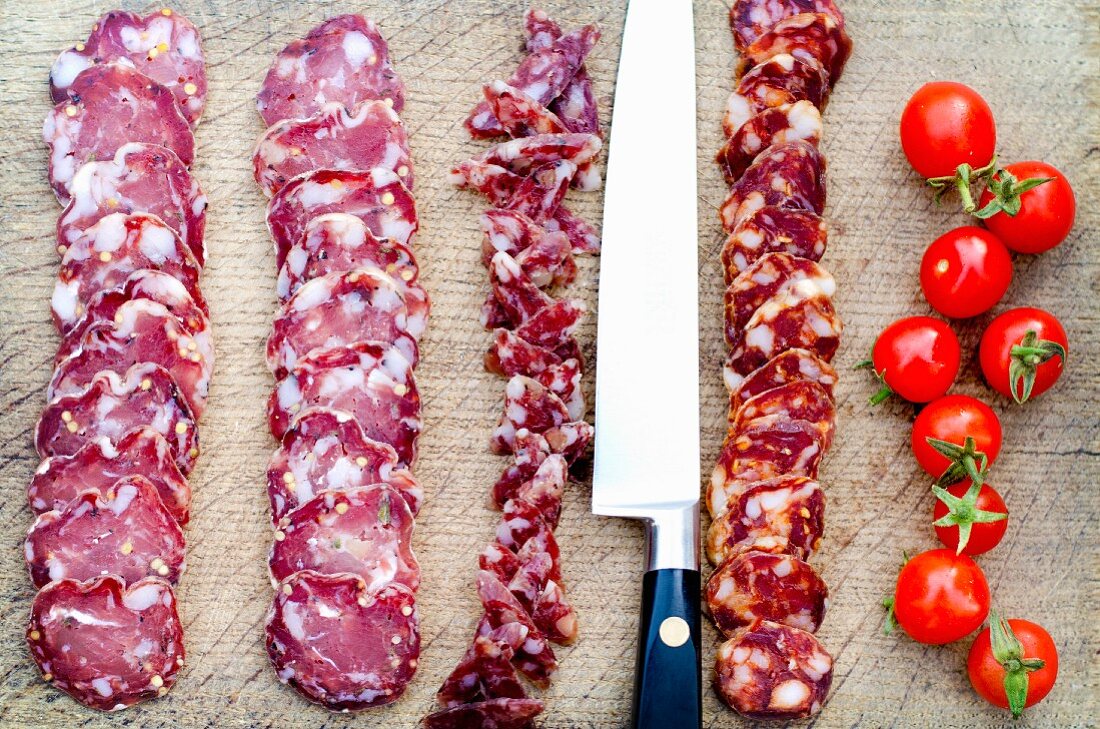 Salami- und Chorizoscheiben mit Messer und Kirschtomaten auf Schneidebrett