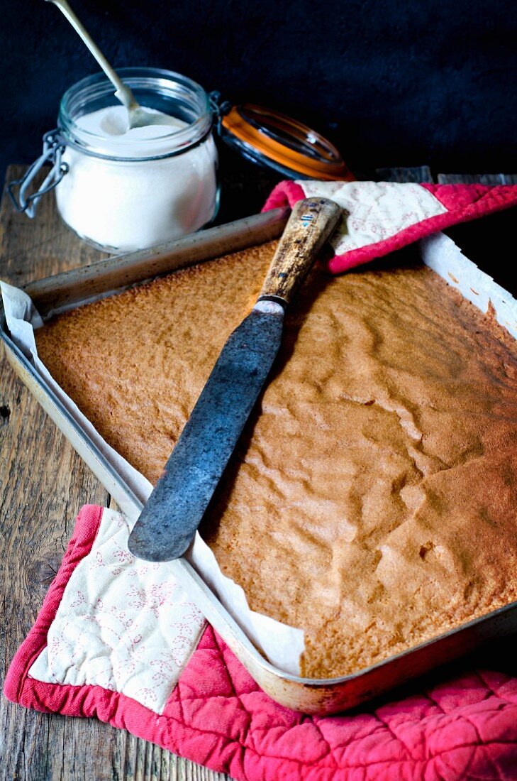 A sponge tray bake cake with a knife and sugar