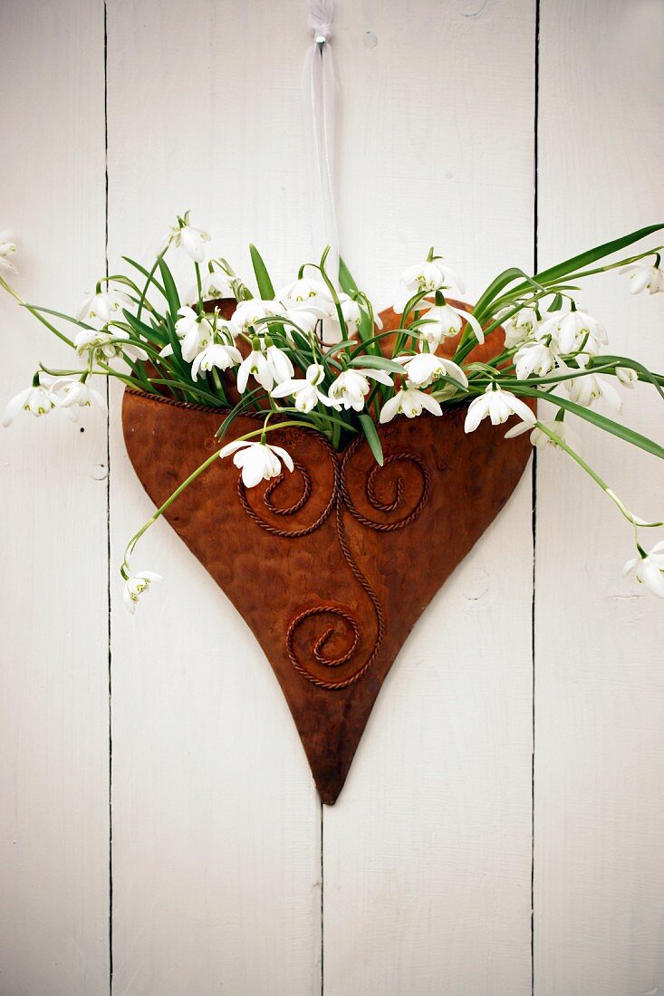Spring wall decoration with snowdrops in heart-shaped vessel