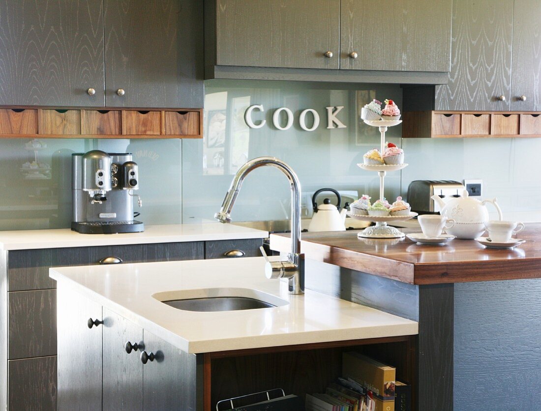 Sink cabinet built abutting kitchen counter in front of fitted cabinets with integrated glass splashback