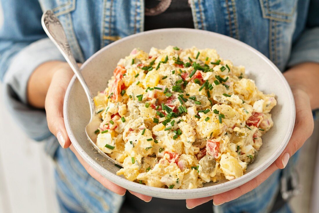 A woman holding a bowl of potato salad with gherkins, peppers, Gouda and mayonnaise