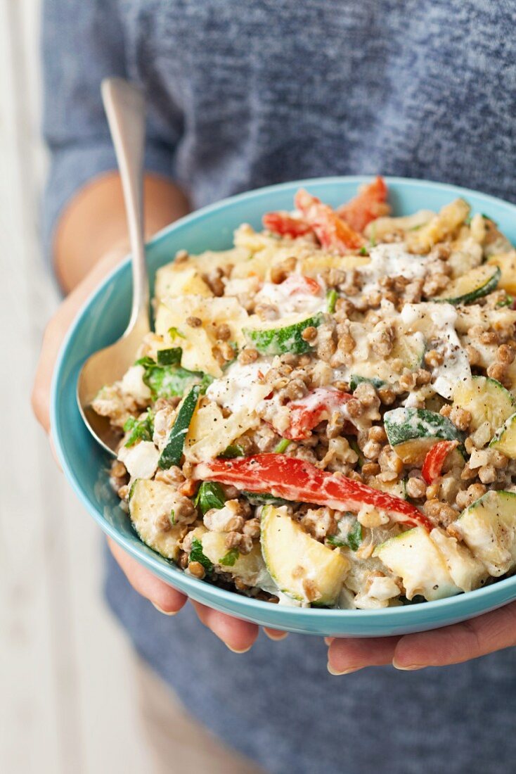 Frau hält eine Schüssel Kartoffelsalat mit Linsen, Paprika, Zucchini und Joghurtdressing