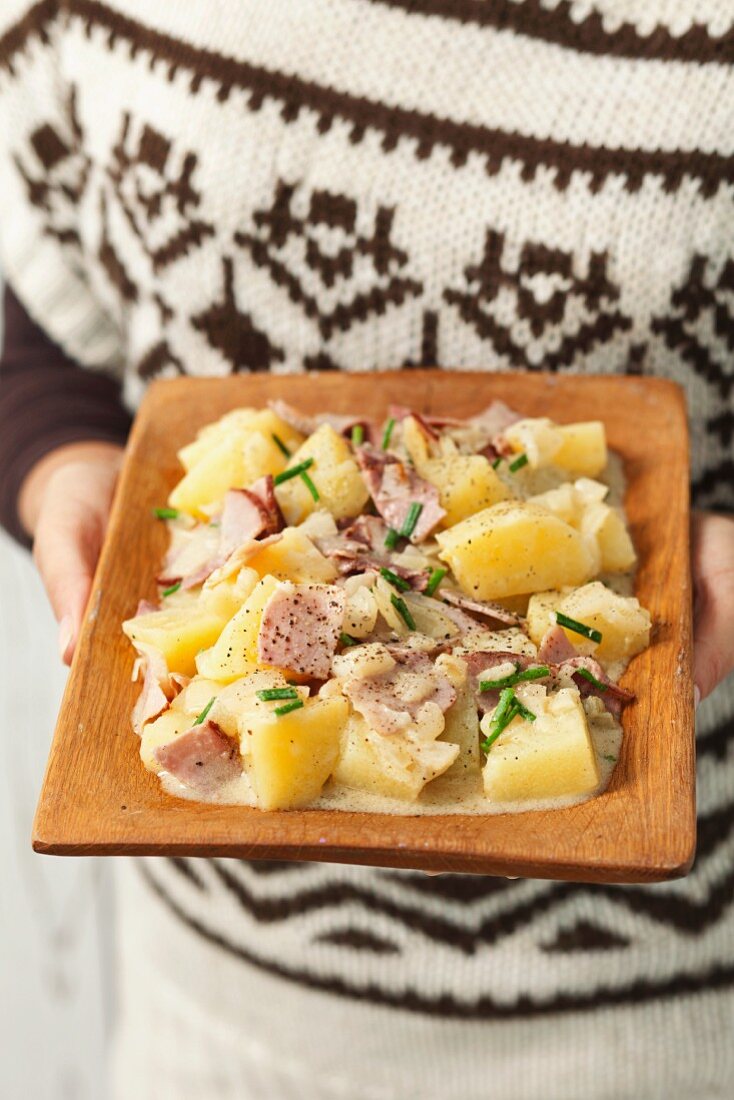 Frau hält einen Teller Kartoffelsalat mit Schinken, Zwiebeln und Sahnedressing