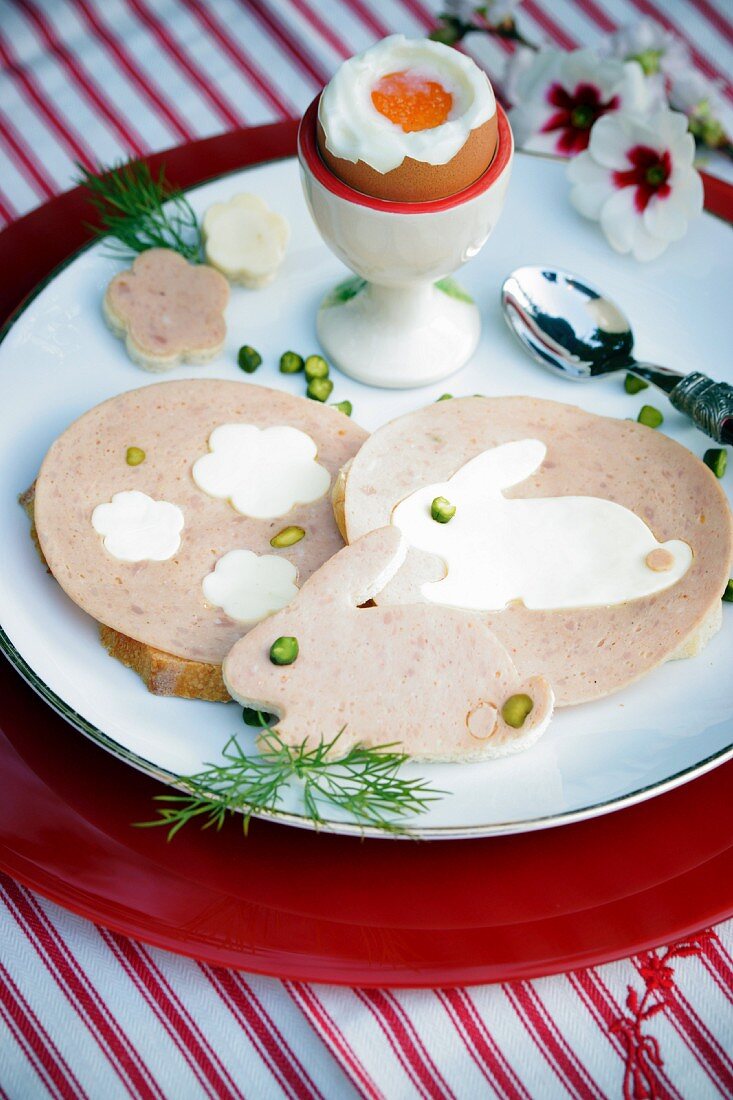 A breakfast platter with a boiled egg, and Easter sausage meat with rabbits and flowers