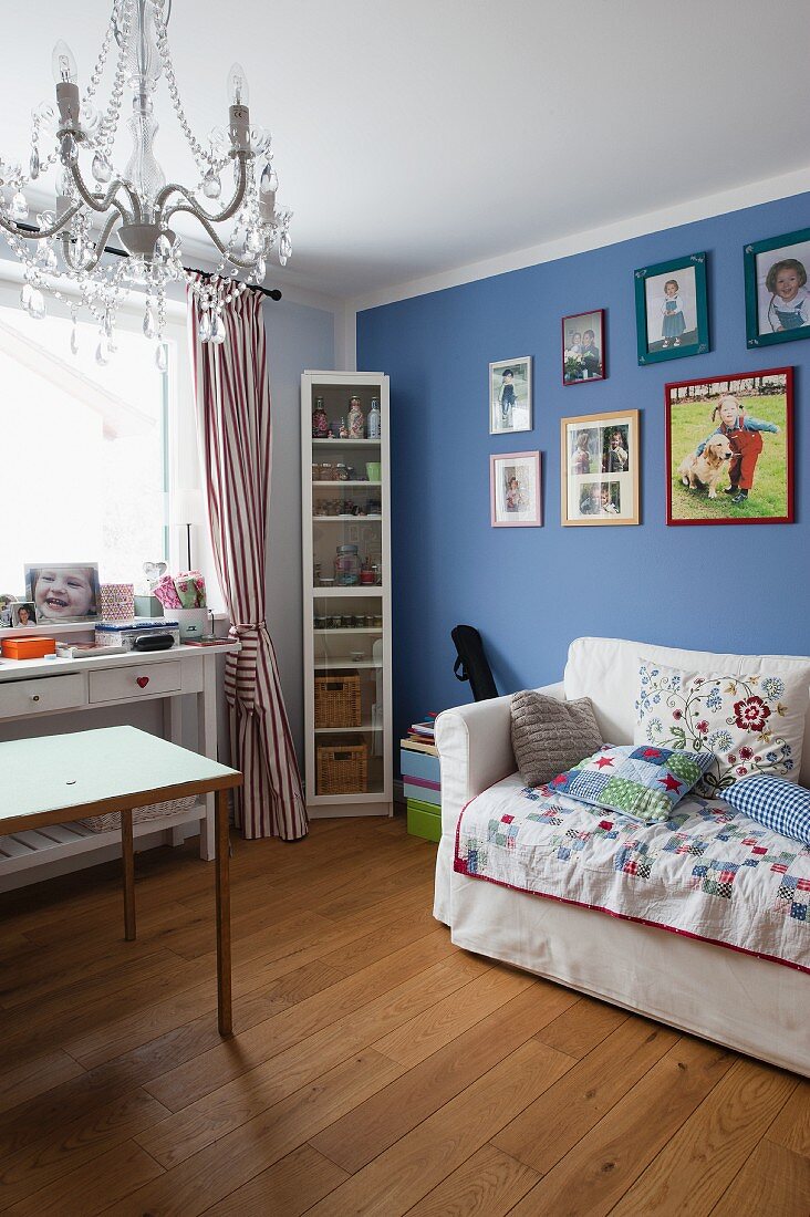 Armchair bed with scatter cushions below framed pictures on blue-painted wall, desk below window