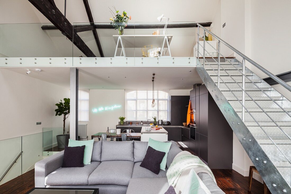 Grey corner sofa and gallery with metal staircase in open-plan, loft-style interior