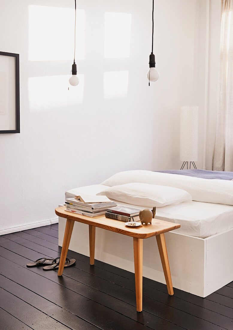 Bedroom with dark wood floor, pendant lamp with pull switch and wooden bench used as bedside table for DIY bed