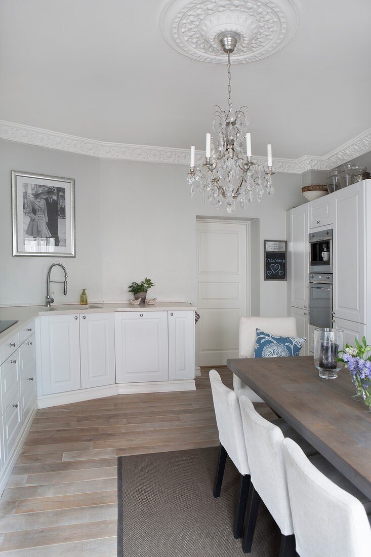 White country-house kitchen and modern dining area in period apartment with chandelier hanging from stucco ceiling rose