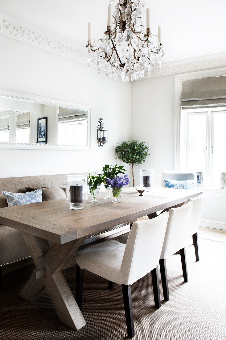 Comfortable dining area with chandelier above solid wood table and simple upholstered furnishings in kitchen-dining room