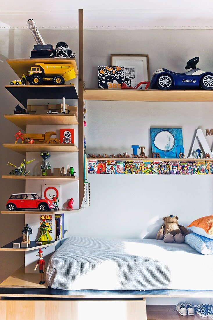 Toys on L-shaped shelves above mattress on wooden base in child's bedroom