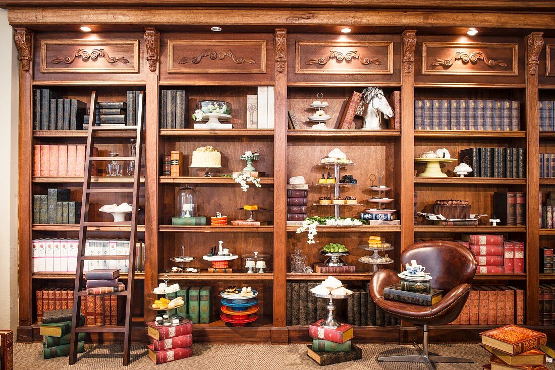 Antique-style, fitted shelves of antiquarian books, cake stands and cake platters