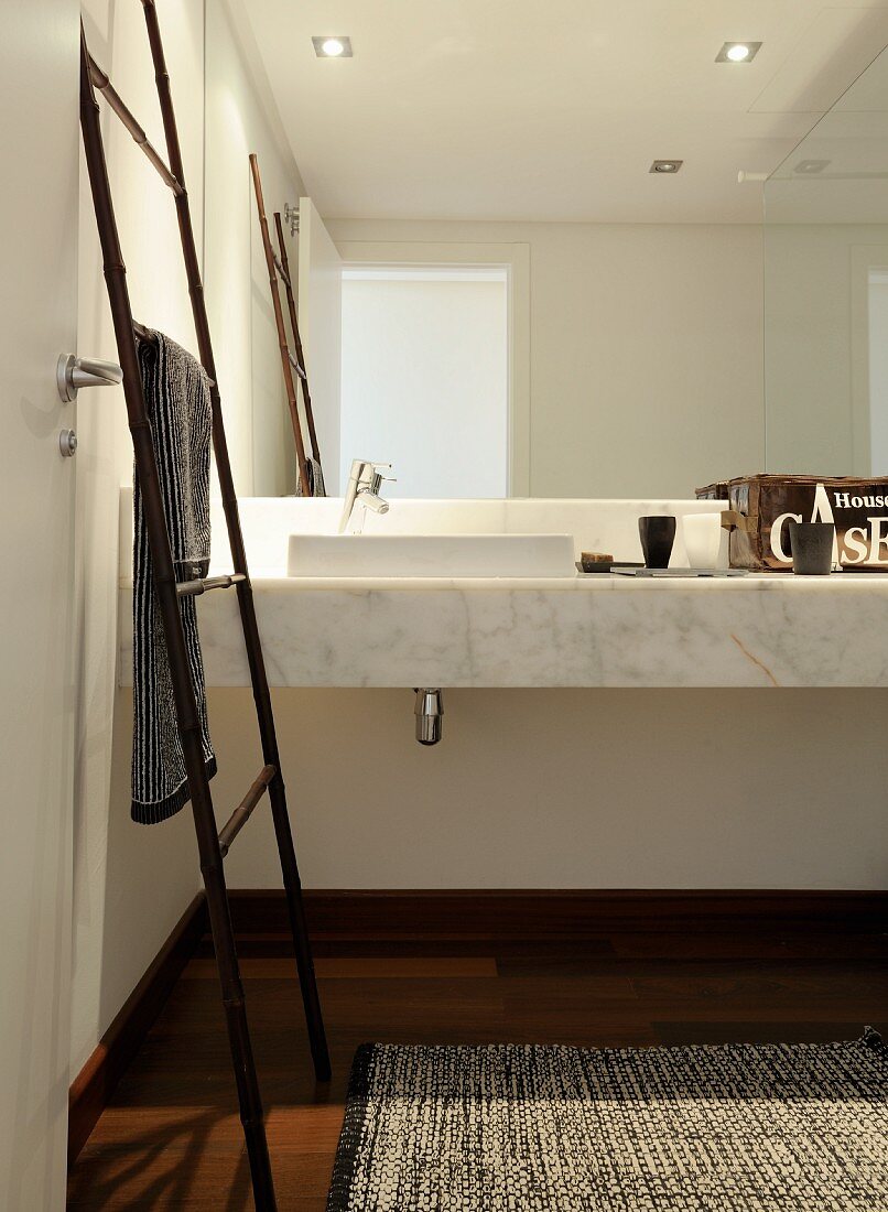 Bamboo, ladder-style towel rack in front of marble washstand and mirrored wall