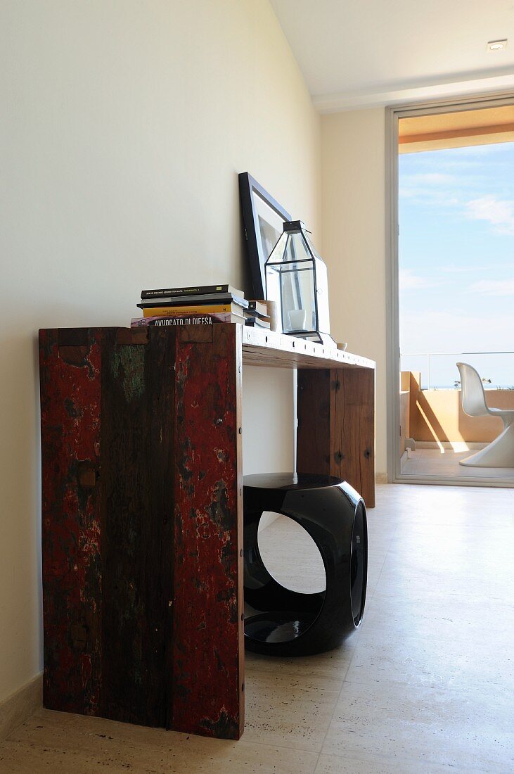 Console table with peeling paint and plastic cube stool; terrace with sea view in background