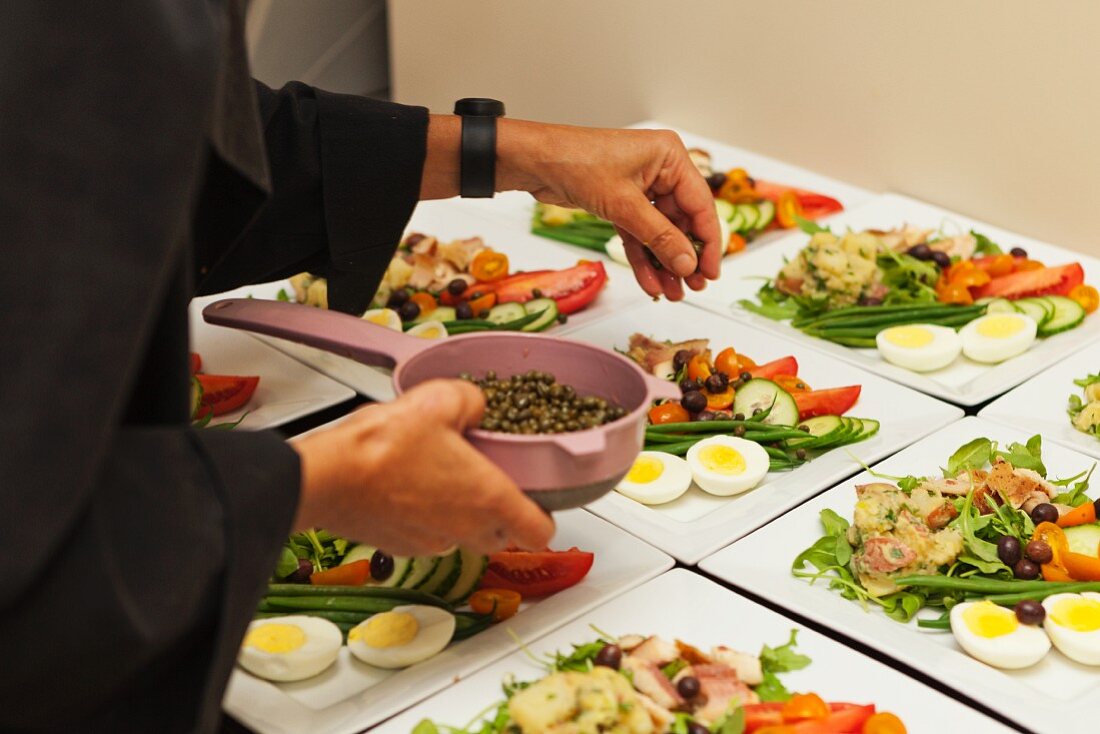 A woman sprinkling capers onto Nicoise salad