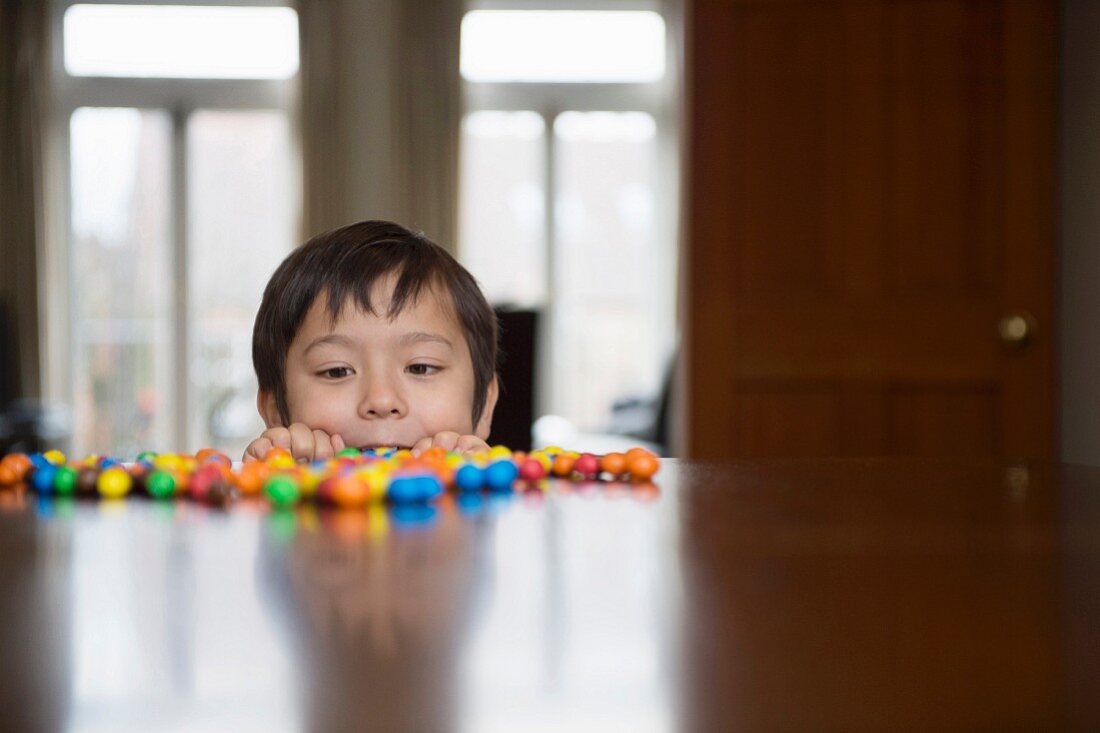 A boy peering over the edge of a table at sweets