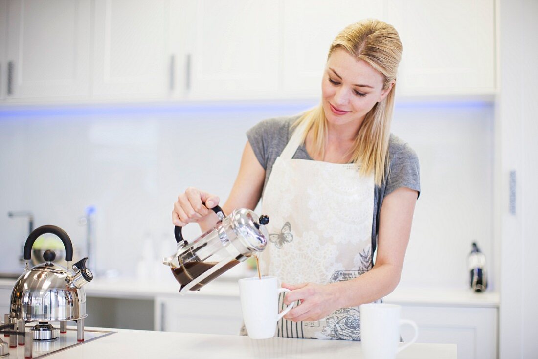A young woman pouring coffee from a French press into a cup