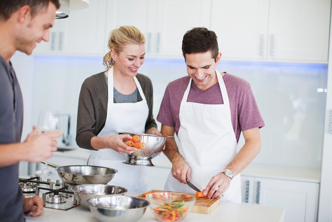 Friends cooking together in a kitchen with a man cutting carrots