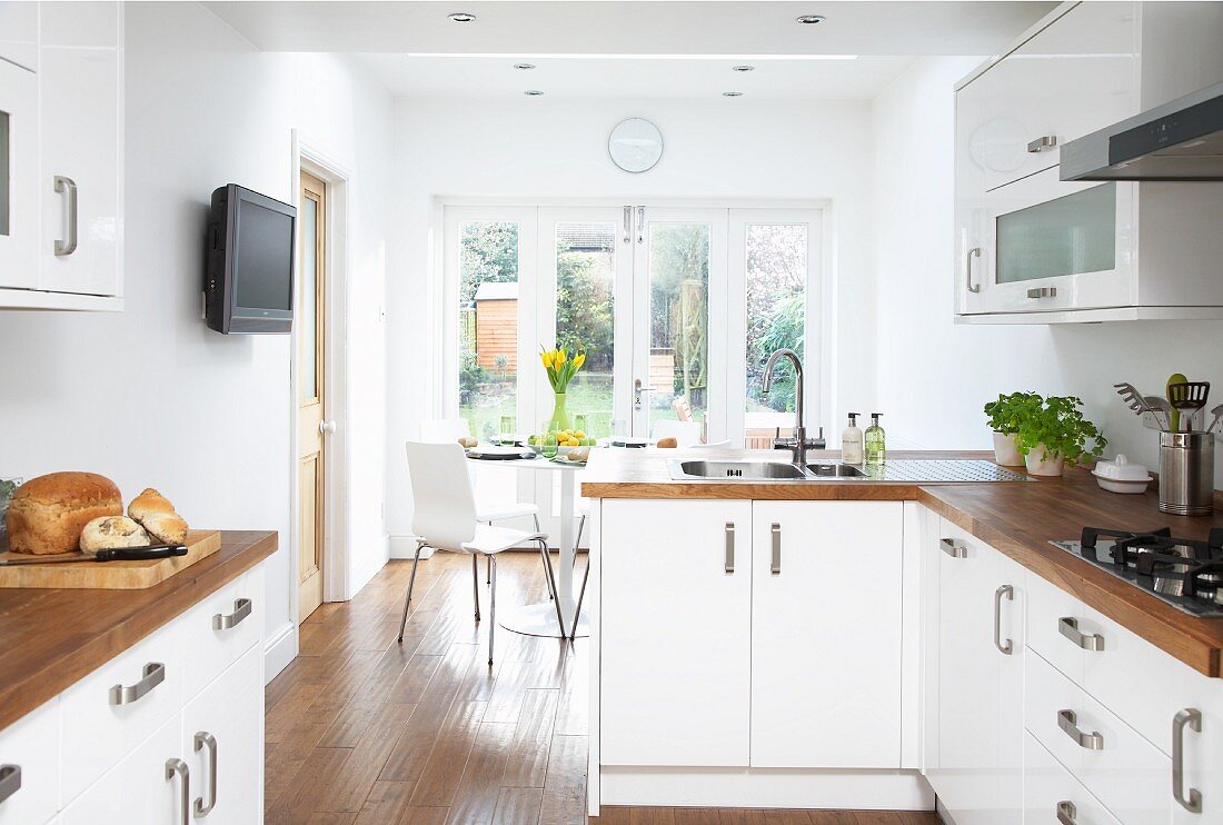 Open-plan fitted kitchen with white fronts and wooden work surfaces; dining area with French windows leading to garden