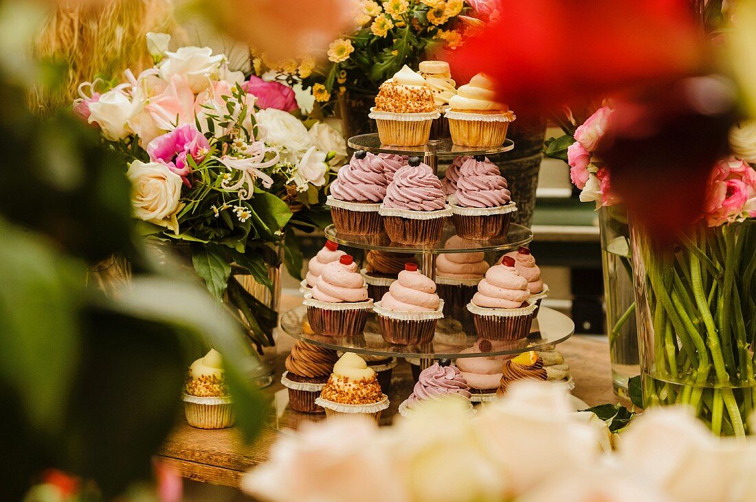 Etagere mit verschiedenen Cupcakes inmitten von Blumen