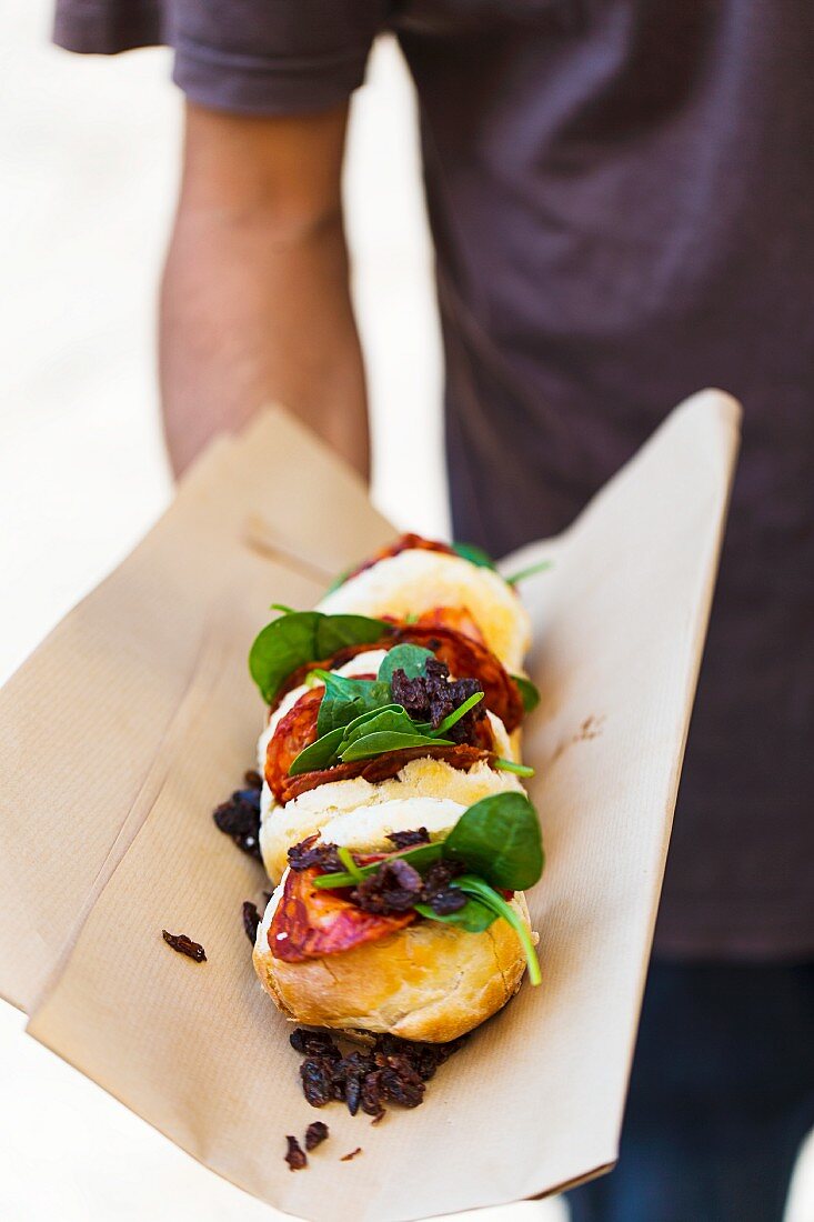 A man holding chorizo and spinach sandwiches