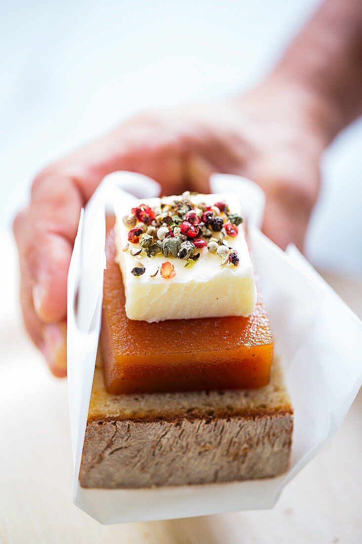A hand holding cornbread with cheese and quince jelly