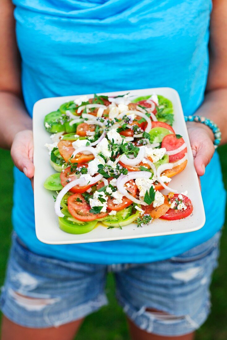 A woman holding a plate of Greek salad