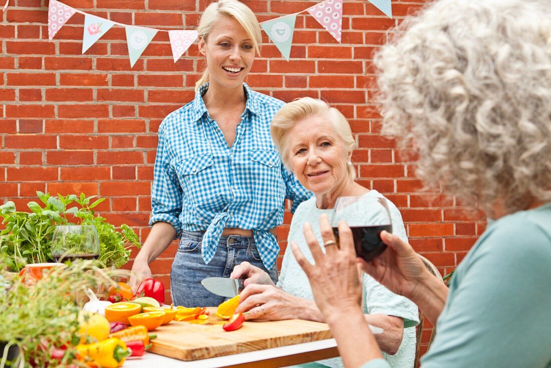 Drei Frauen unterschiedlichen Alters unterhalten sich während der Zubereitung von Speisen am Gartentisch