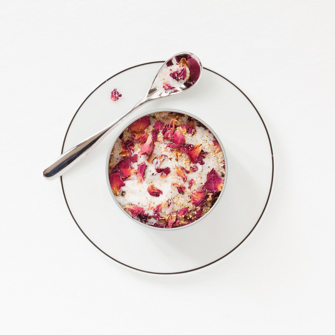 A tin of rose scented sugar on a plate with a spoon