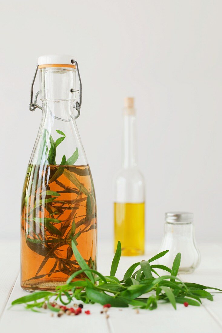 A bottle of tarragon vinegar, fresh tarragon and peppercorns