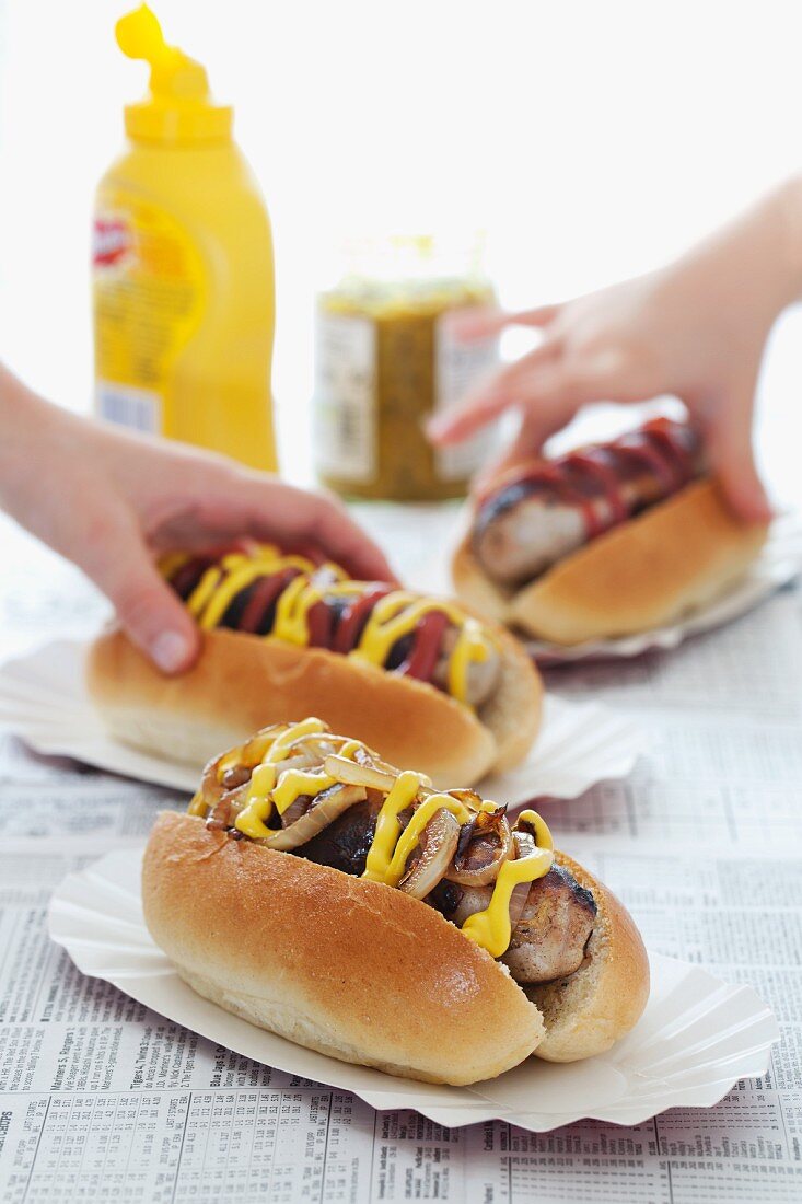 Children's hands taking hot dogs with mustard and ketchup
