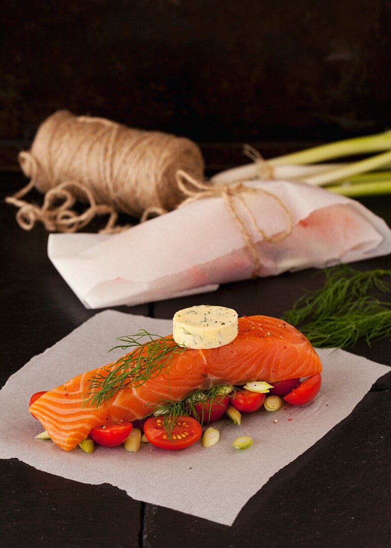 Salmon fillet with dill butter, tomatoes and spring onion on parchment paper