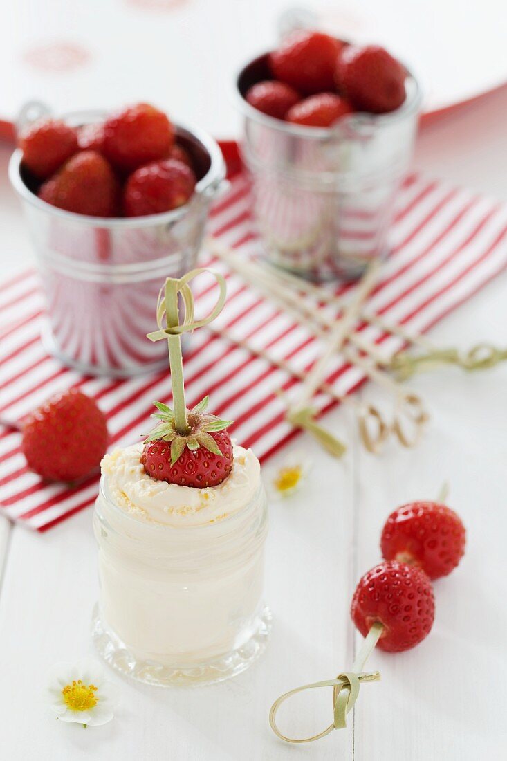 A strawberry skewer dipped in a jar of clotted cream