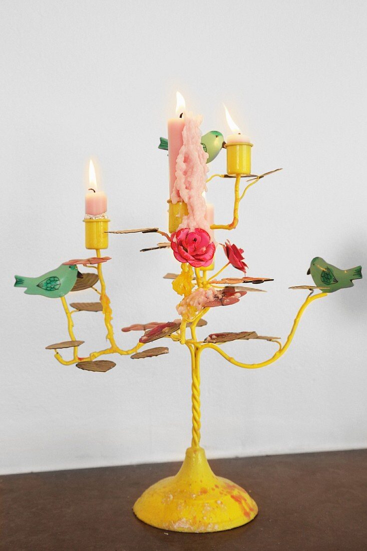 Lit candles in yellow-painted, romantic candlestick decorated with bird and flower ornaments