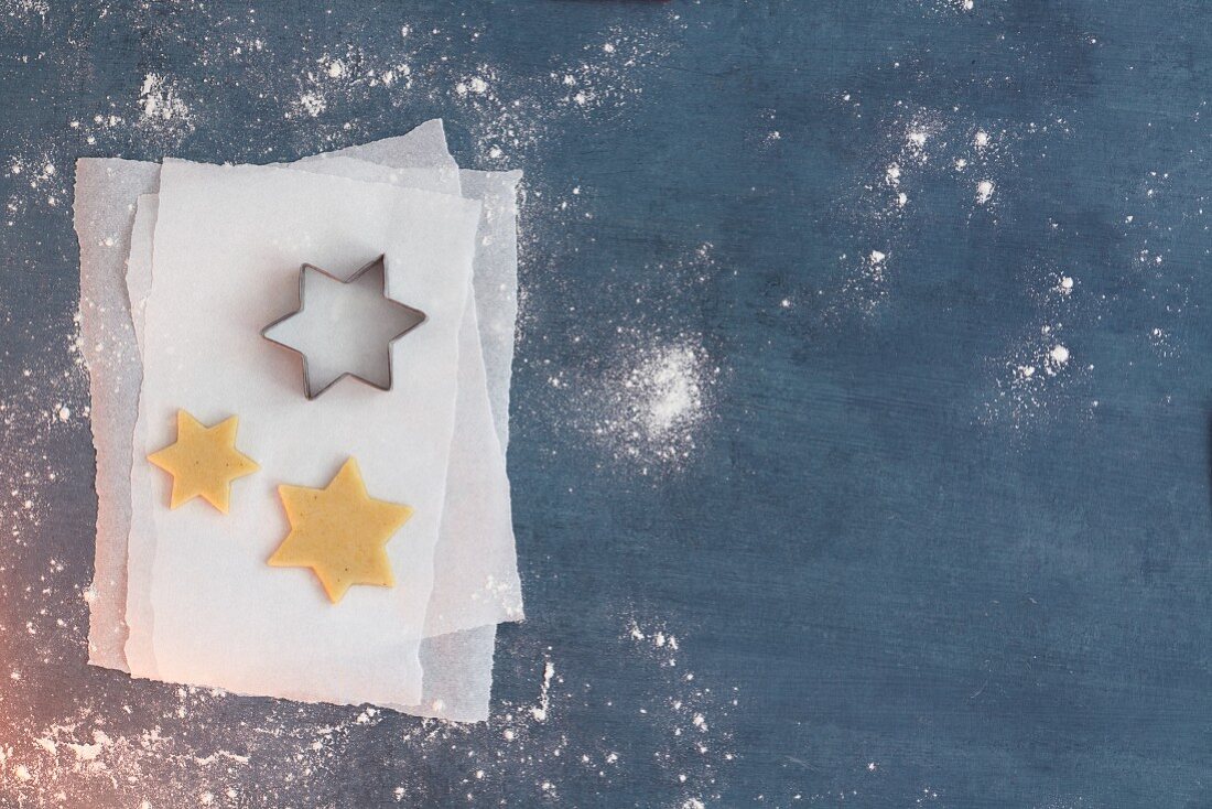 Unbaked star-shaped biscuits and a star-shaped cutter on a piece of parchment paper