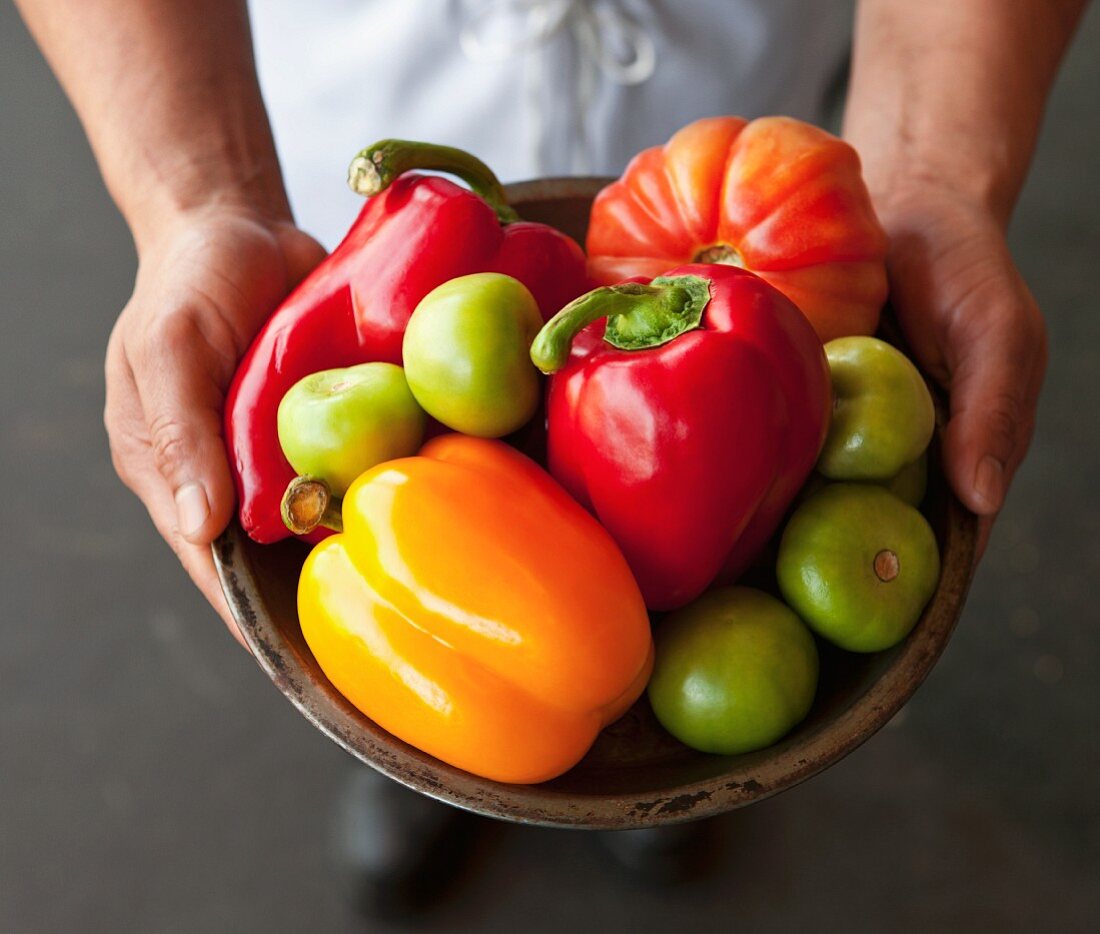 Koch hält eine Schüssel mit Paprika, Tomatillos und Tomate