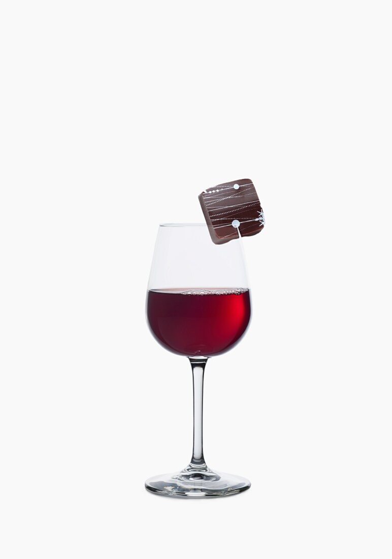 A chocolate praline on the rim of a glass of red wine