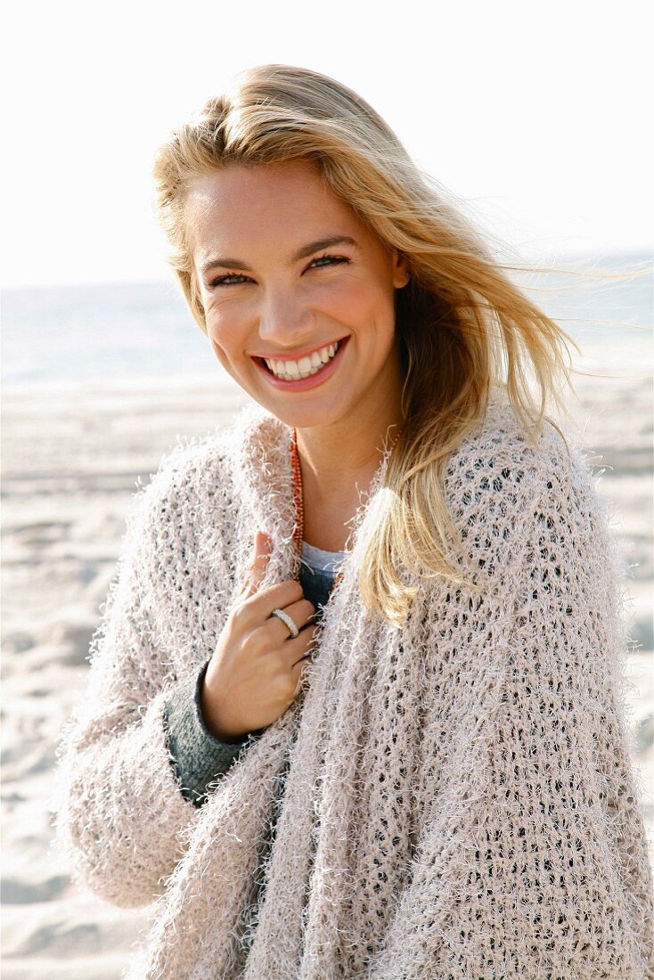 Junge, blonde Frau in beigefarbener Strickjacke am Meer