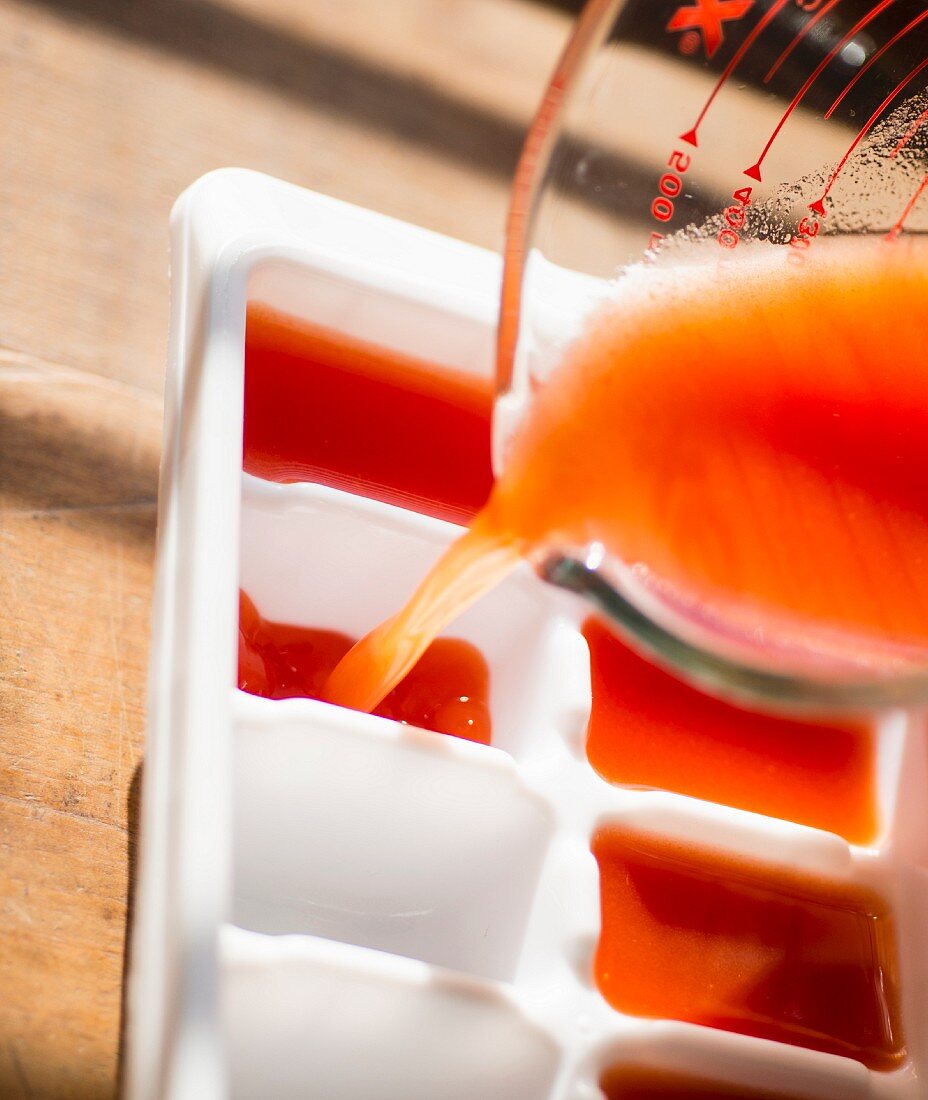 Tomato juice being poured into an ice cube tray to be frozen