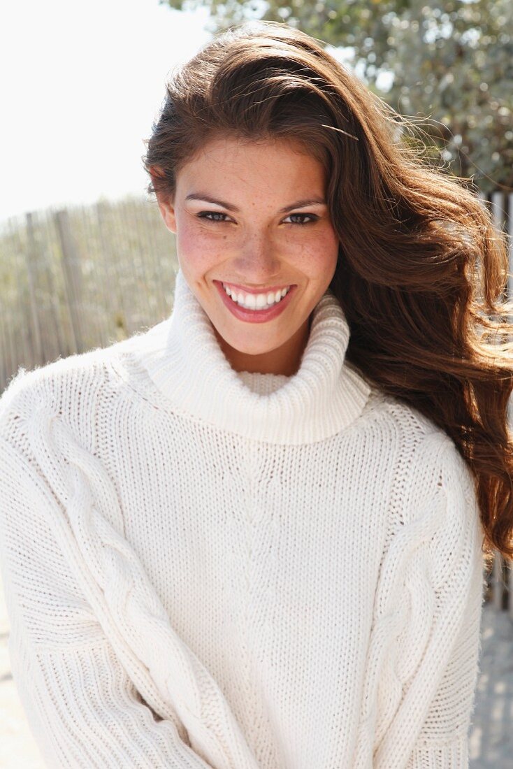 A young brunette woman outside wearing a white knitted roll-neck jumper