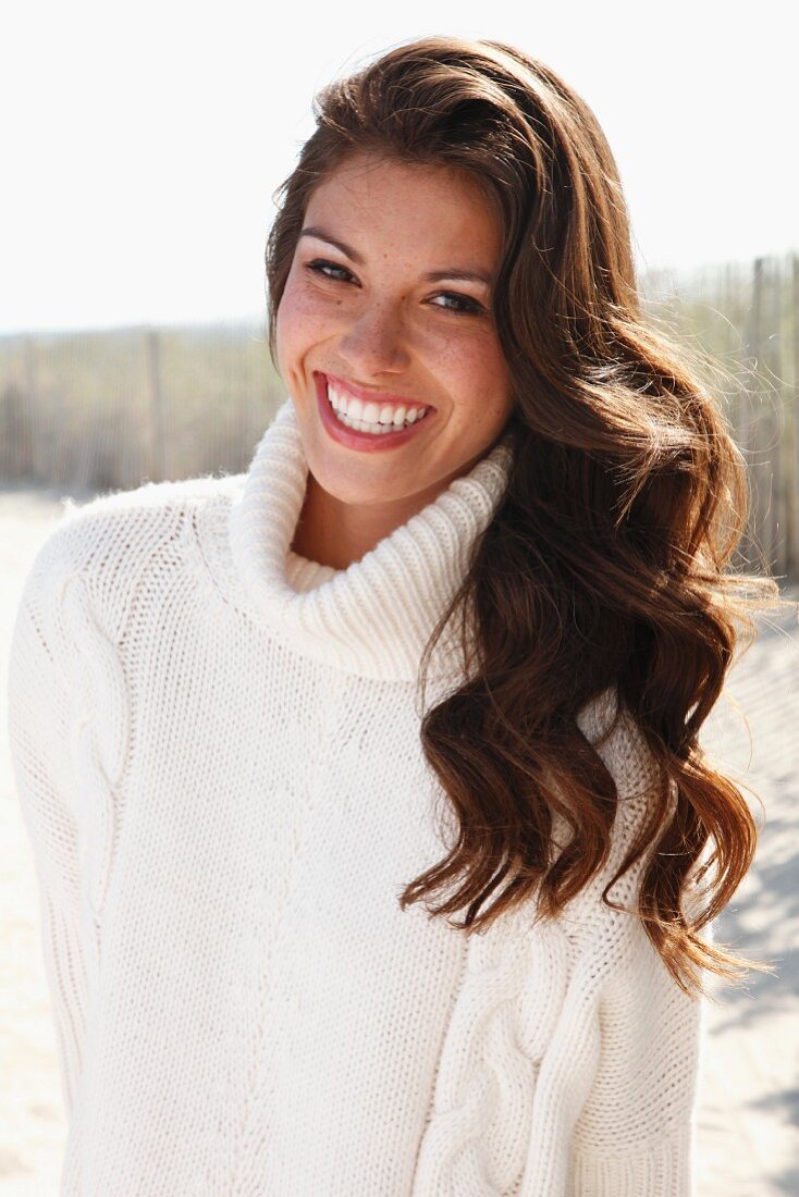 A young brunette woman outside wearing a white knitted roll-neck jumper