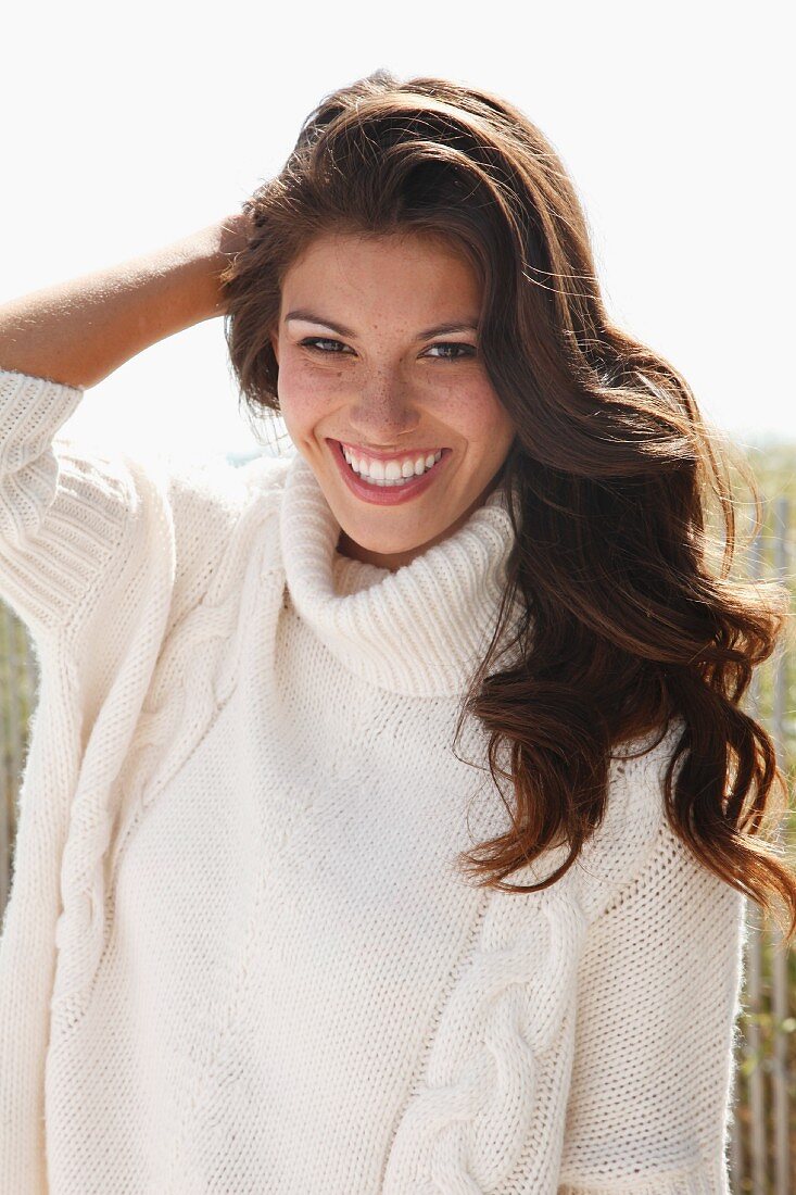 A young brunette woman outside wearing a white knitted roll-neck jumper
