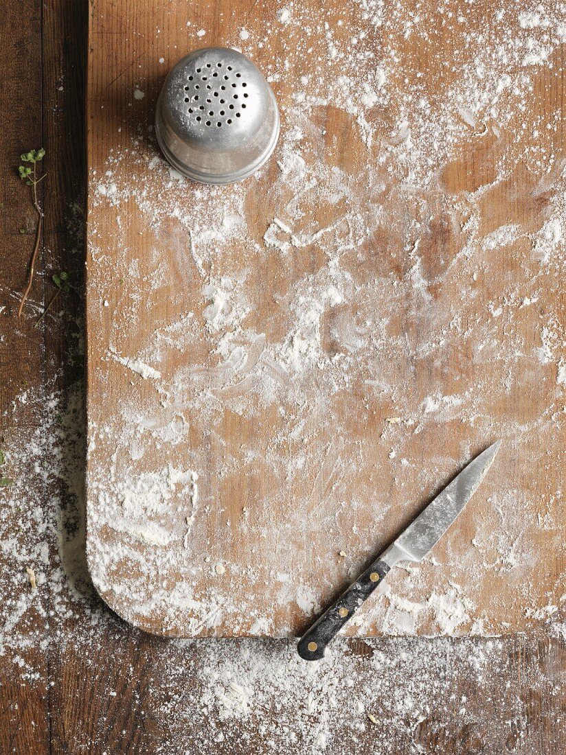 Flour and a knife on a chopping board (seen from above)