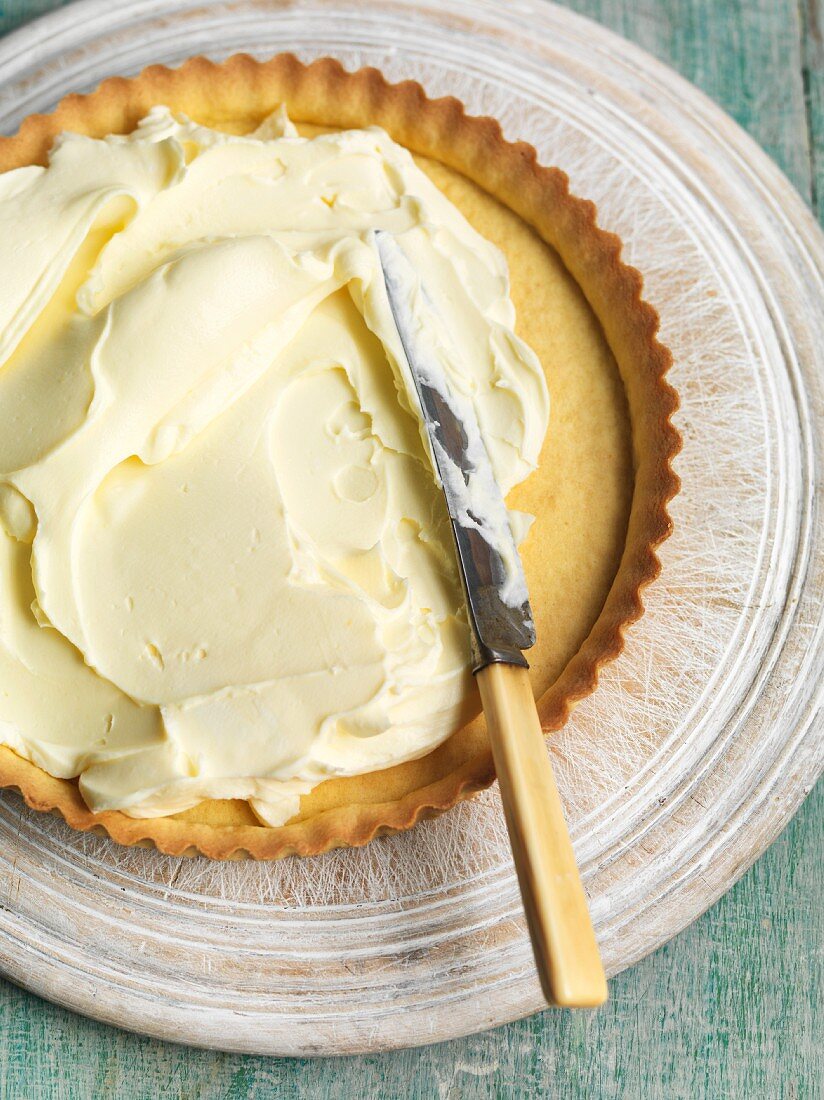 Mascarpone and lemon curd cream being spread on a shortcrust tart base