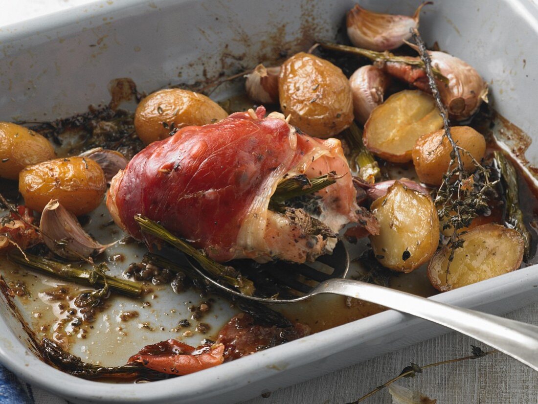 Chicken breast stuffed with asparagus wrapped in Parma ham in a roasting tin with new potatoes, garlic and thyme