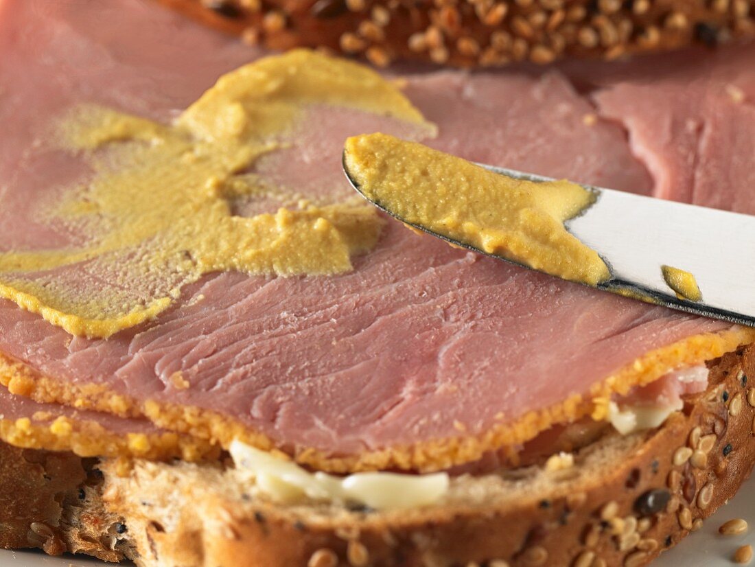 Mustard being spread on a ham sandwich (close-up)